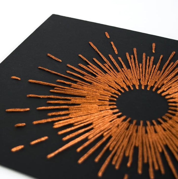 Black paper with copper sunburst design on a white background