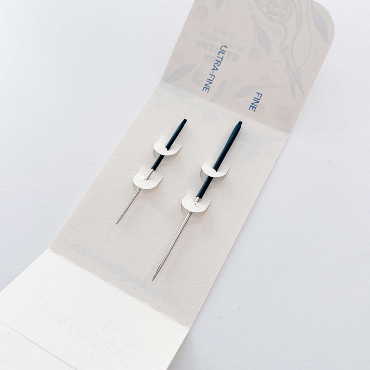 Two black and silver needles on a white background with a beige case labeled 'Ultra-Fine' and 'Fine'.