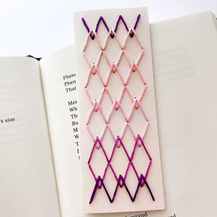 Embroidered bookmark with pink and purple pattern on a book page