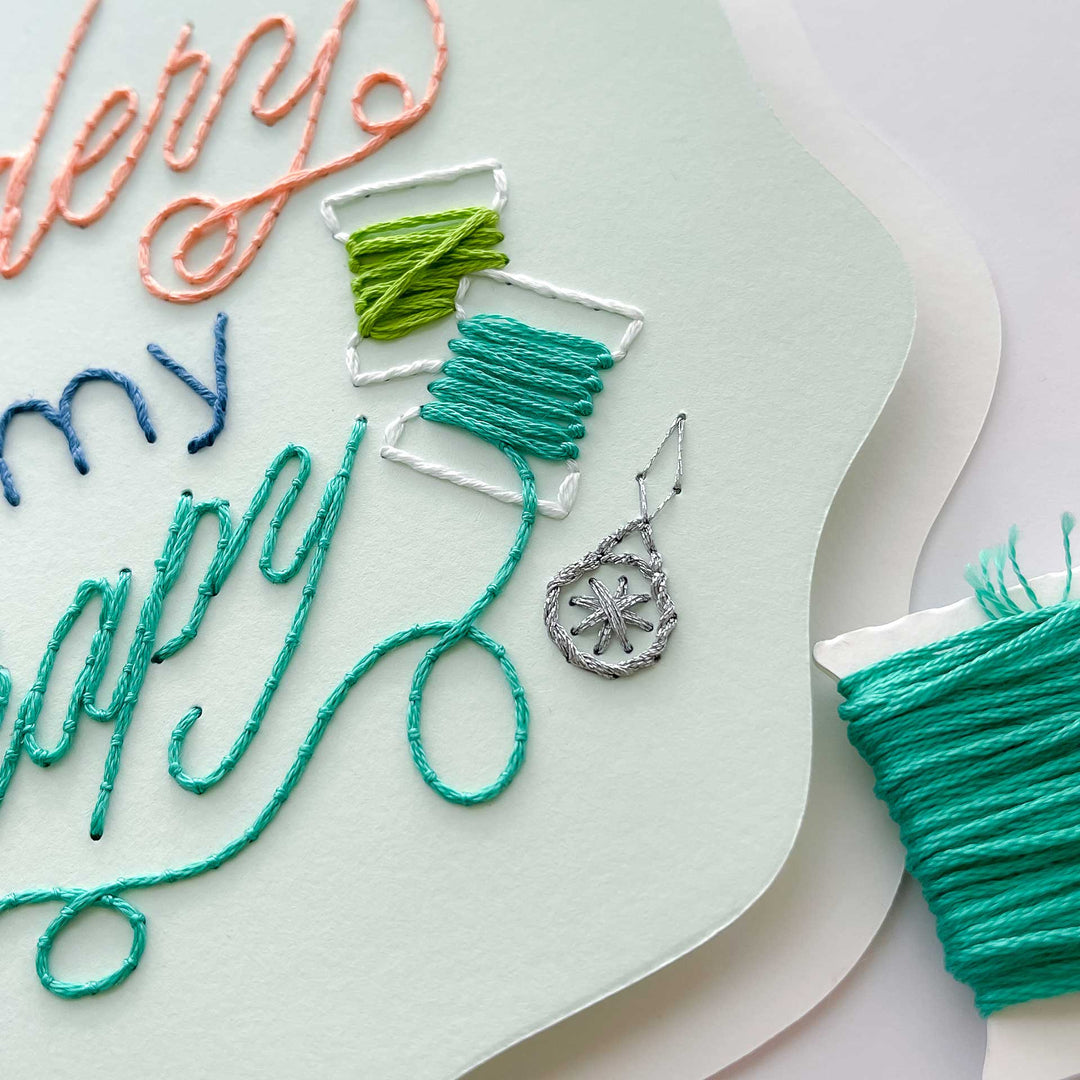 Embroidery paper with colorful thread and a pendant on a light green background