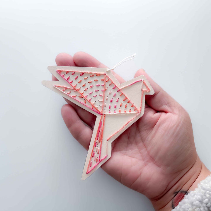 Hand holding a geometrically shaped pink and white object against a white background