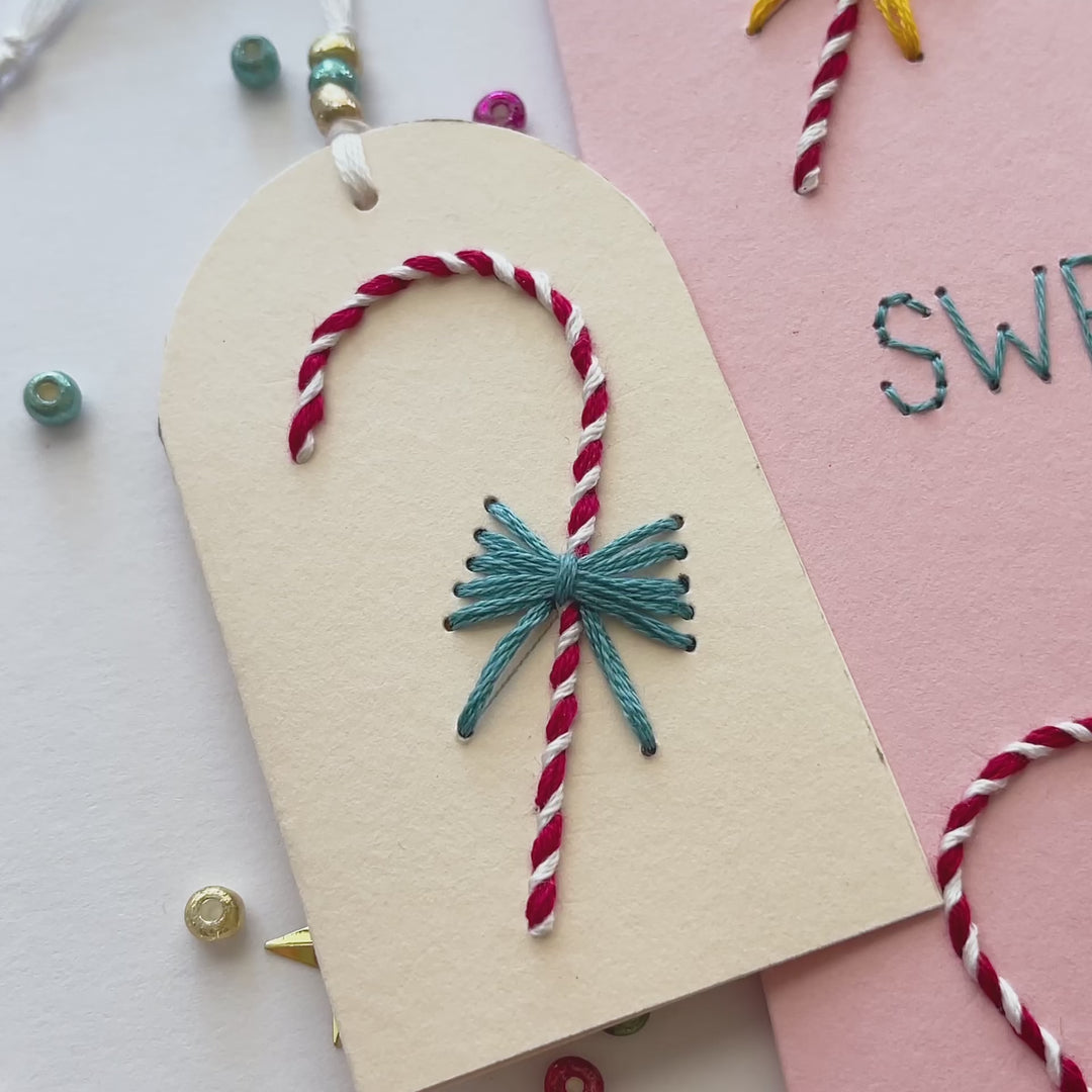 Video showcase of the completed hand-embroidered "Sweet Christmas Wishes" card and matching gift tag, displaying the stitched red and white candy canes and colorful thread bow details.